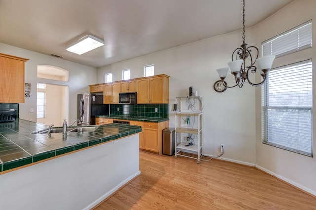 7515 N Wheeler Ave, Fresno, CA 93722 - kitchen with black microwave, freestanding refrigerator, tile countertops, light wood finished floors, and backsplash