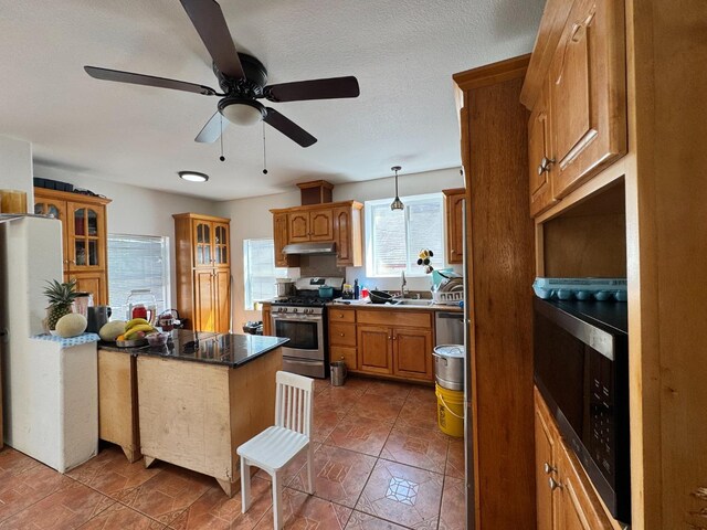 1925 E 15th, Oakland, CA 94606 - kitchen with gas stove, under cabinet range hood, brown cabinets, glass insert cabinets, and a ceiling fan