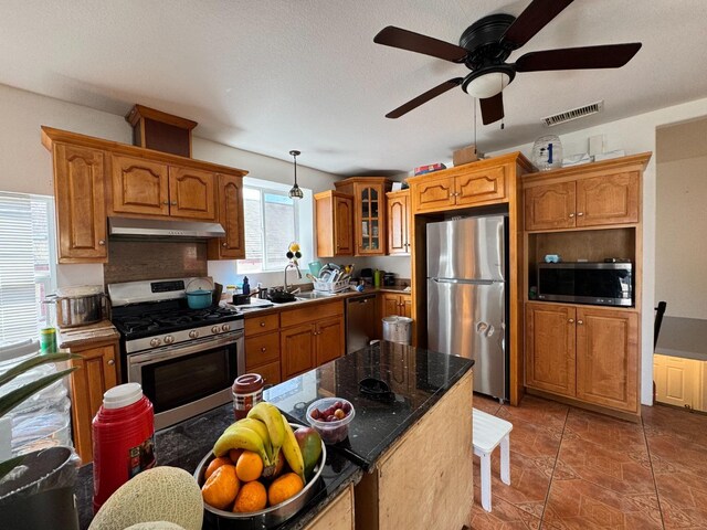 1925 E 15th, Oakland, CA 94606 - kitchen featuring stainless steel appliances, under cabinet range hood, a ceiling fan, brown cabinetry, and glass insert cabinets