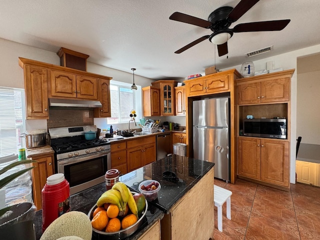 1925 E 15th, Oakland, CA 94606 - kitchen featuring stainless steel appliances, under cabinet range hood, a ceiling fan, brown cabinetry, and glass insert cabinets