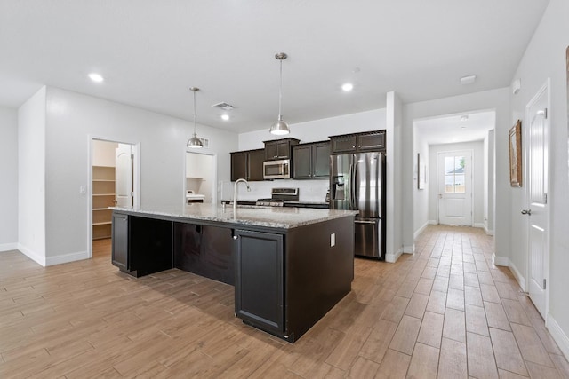 2456 Junipero Ave, Clovis, CA 93619 - kitchen with appliances with stainless steel finishes, light wood finished floors, a kitchen island with sink, light stone countertops, and recessed lighting