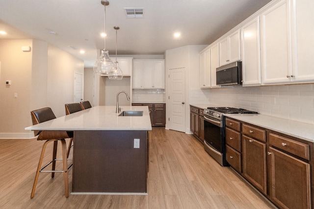 153 N Bliss Ave, Fresno, CA 93727 - kitchen with appliances with stainless steel finishes, light wood-style flooring, white cabinets, a kitchen breakfast bar, and decorative backsplash