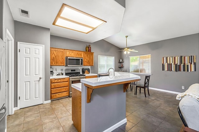 205 N Douglas Ave, Fresno, CA 93727 - kitchen with appliances with stainless steel finishes, tile countertops, vaulted ceiling, a kitchen breakfast bar, and a kitchen island with sink