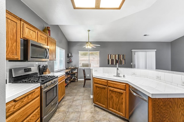 205 N Douglas Ave, Fresno, CA 93727 - kitchen featuring stainless steel appliances, tile countertops, backsplash, lofted ceiling, and brown cabinets