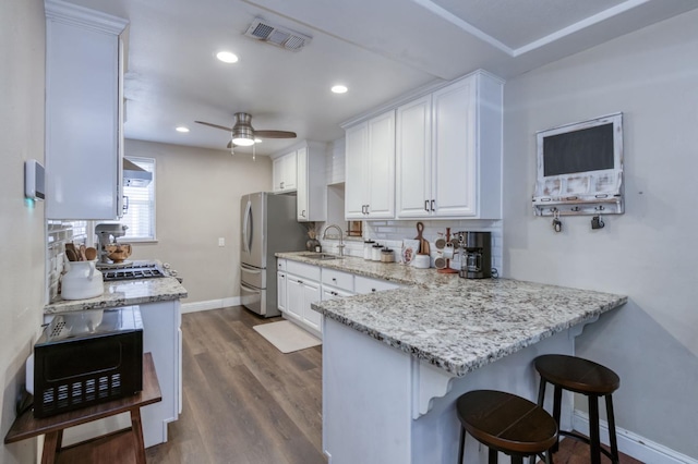 3054 E Brown Ave, Fresno, CA 93703 - kitchen with freestanding refrigerator, white cabinetry, backsplash, a kitchen breakfast bar, and light stone counters