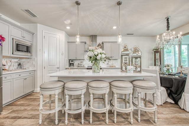 1363 E Via Prato Dr, Fresno, CA 93730 - kitchen featuring stainless steel microwave, tasteful backsplash, light countertops, light wood finished floors, and a kitchen bar