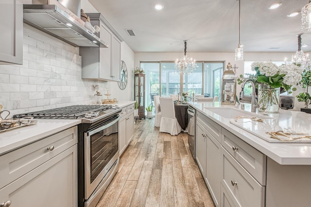 1363 E Via Prato Dr, Fresno, CA 93730 - kitchen with appliances with stainless steel finishes, wall chimney range hood, a chandelier, light wood-style flooring, and light countertops