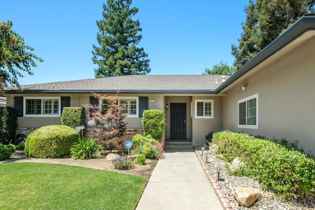 3218 E Ellery Ave, Fresno, CA 93710 - view of exterior entry with stucco siding, a lawn, roof with shingles, and brick siding