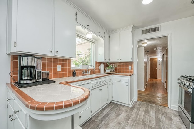 3625 E Cortland Ave, Fresno, CA 93726 - kitchen featuring stainless steel range with gas stovetop, tile counters, light wood-style floors, white cabinets, and tasteful backsplash