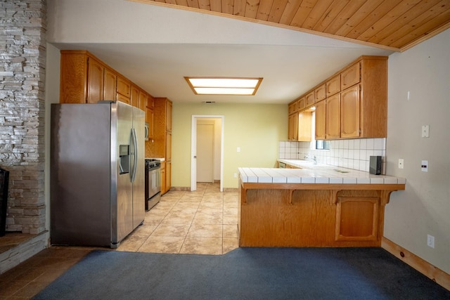 38475 Sierra Lakes Dr, Oakhurst, CA 93644 - kitchen with appliances with stainless steel finishes, a peninsula, tile counters, a kitchen bar, and decorative backsplash
