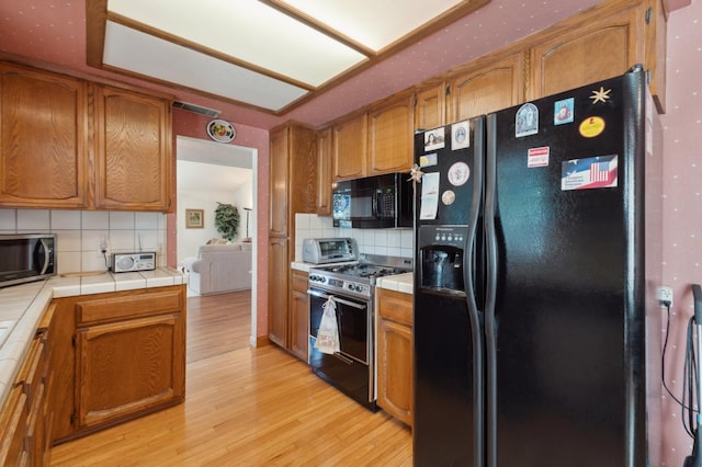 1059 E Fallbrook Ave, Fresno, CA 93720 - kitchen featuring black appliances, tile countertops, decorative backsplash, and light wood-style flooring