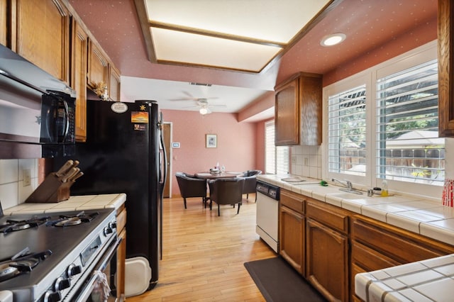 1059 E Fallbrook Ave, Fresno, CA 93720 - kitchen with white dishwasher, gas range, tile countertops, black microwave, and light wood-style flooring