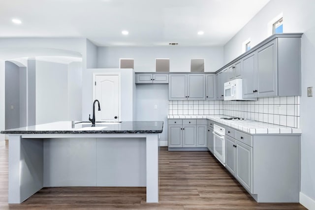 5667 W Bluff Ave, Fresno, CA 93722 - kitchen featuring arched walkways, white appliances, a center island with sink, wood finished floors, and recessed lighting