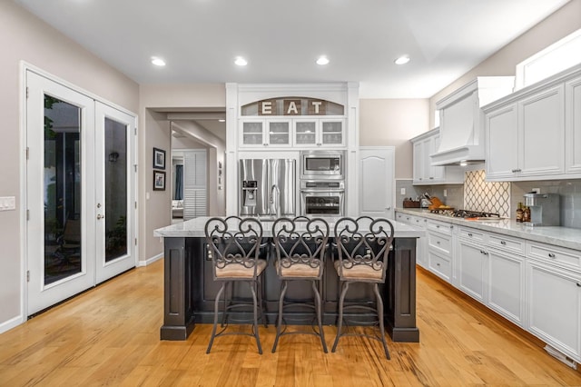 2143 Everglade Ave, Clovis, CA 93619 - kitchen featuring appliances with stainless steel finishes, a breakfast bar area, an island with sink, tasteful backsplash, and light wood-style flooring