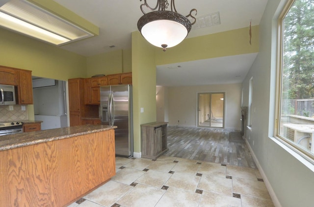 10521 N Doheny Ave, Fresno, CA 93730 - kitchen featuring appliances with stainless steel finishes, brown cabinets, backsplash, hanging light fixtures, and dark countertops