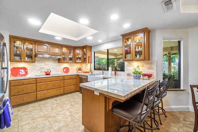 1721 W Wrenwood Ave, Fresno, CA 93711 - kitchen with brown cabinetry, a peninsula, decorative backsplash, a kitchen bar, and recessed lighting