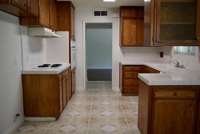 6061 N 9th St, Fresno, CA 93710 - kitchen featuring under cabinet range hood, white appliances, tasteful backsplash, brown cabinetry, and tile counters