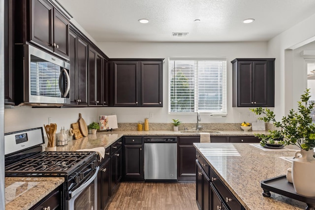 7141 N Shiraz Ave, Fresno, CA 93722 - kitchen featuring appliances with stainless steel finishes, light stone counters, wood finished floors, recessed lighting, and dark brown cabinetry