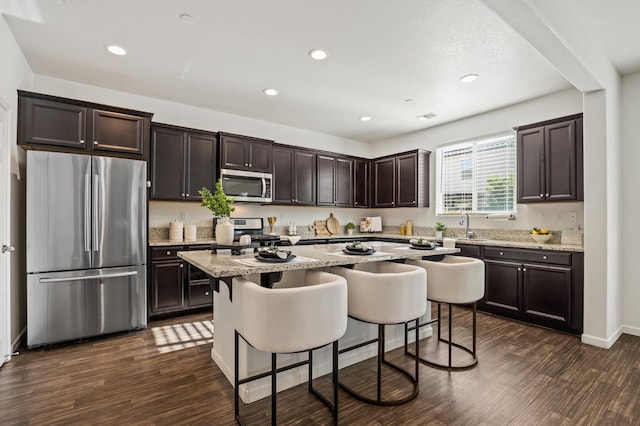 7141 N Shiraz Ave, Fresno, CA 93722 - kitchen with stainless steel appliances, dark brown cabinets, a kitchen island, a kitchen bar, and dark wood-style floors