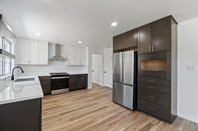 19730 Brightwood Rd, Madera, CA 93638 - kitchen featuring appliances with stainless steel finishes, wall chimney range hood, light wood finished floors, dark brown cabinetry, and white cabinetry