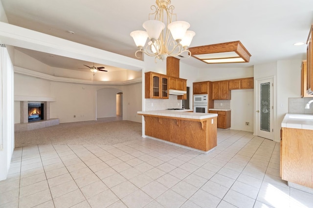 122 E Loop, Madera, CA 93637 - kitchen featuring a peninsula, brown cabinetry, under cabinet range hood, arched walkways, and tile counters