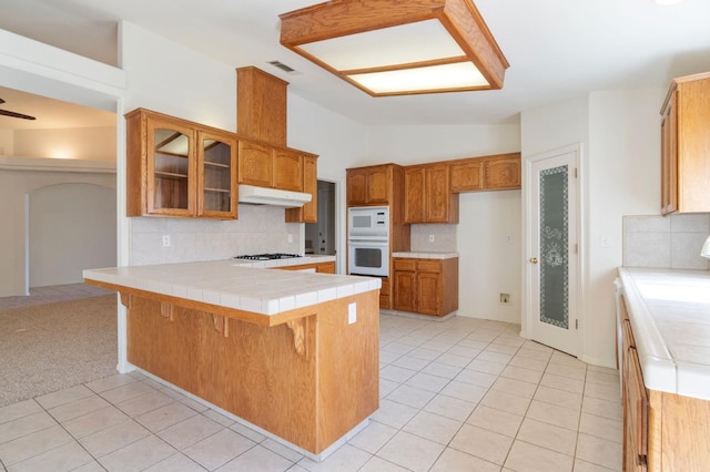 122 E Loop, Madera, CA 93637 - kitchen featuring a peninsula, under cabinet range hood, white microwave, stainless steel gas stovetop, and glass insert cabinets