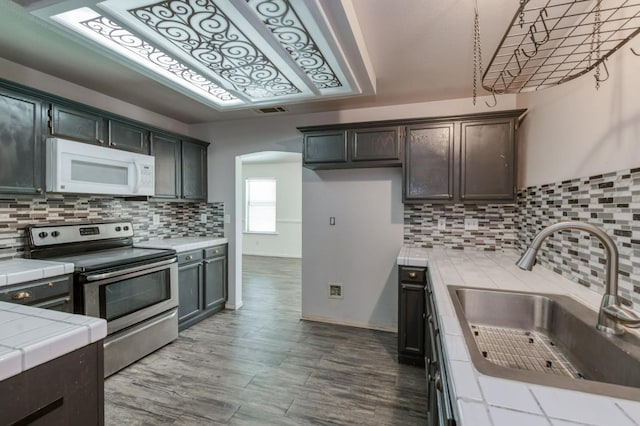 4665 W Yale Ave, Fresno, CA 93722 - kitchen featuring stainless steel range with electric cooktop, tile counters, white microwave, backsplash, and dark brown cabinets