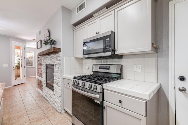 1734 Glen Oban Ln, Clovis, CA 93619 - kitchen with appliances with stainless steel finishes, tile countertops, decorative backsplash, light tile patterned floors, and a stone fireplace