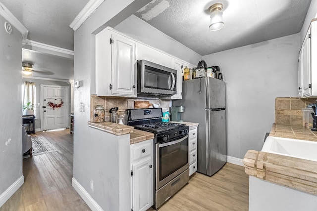 5098 E Ashlan Ave Unit 116, Fresno, CA 93727 - kitchen featuring appliances with stainless steel finishes, light wood-style floors, white cabinetry, decorative backsplash, and ornamental molding