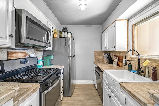 5098 E Ashlan Ave Unit 116, Fresno, CA 93727 - kitchen featuring stainless steel appliances, tile counters, white cabinetry, and light wood-type flooring
