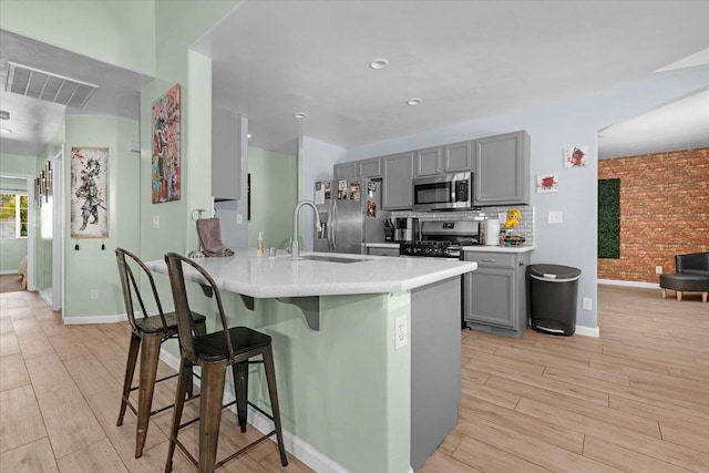 3673 N Denali Ave, Fresno, CA 93727 - kitchen with stainless steel appliances, gray cabinets, a kitchen bar, light wood finished floors, and light countertops
