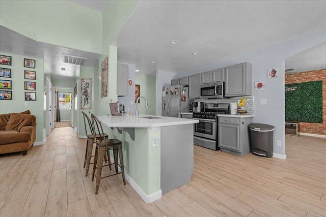 3673 N Denali Ave, Fresno, CA 93727 - kitchen with appliances with stainless steel finishes, gray cabinetry, a breakfast bar area, light wood finished floors, and a peninsula