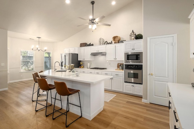 10223 N Price Ave, Fresno, CA 93730 - kitchen with appliances with stainless steel finishes, under cabinet range hood, a breakfast bar, light countertops, and white cabinetry