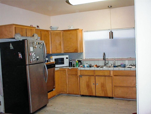 34937 Bronco Ln, Yokuts Valley, CA 93675 - kitchen with freestanding refrigerator, white microwave, light wood-style floors, tile counters, and brown cabinetry