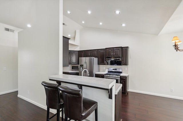 1158 E Hogan Ave, Fresno, CA 93730 - kitchen with stainless steel appliances, dark brown cabinetry, decorative backsplash, a breakfast bar, and dark wood-style flooring