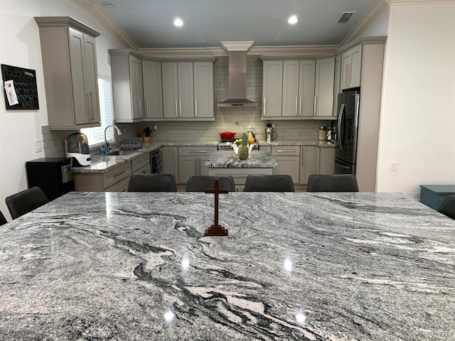kitchen featuring wall chimney range hood, gray cabinetry, freestanding refrigerator, crown molding, and backsplash