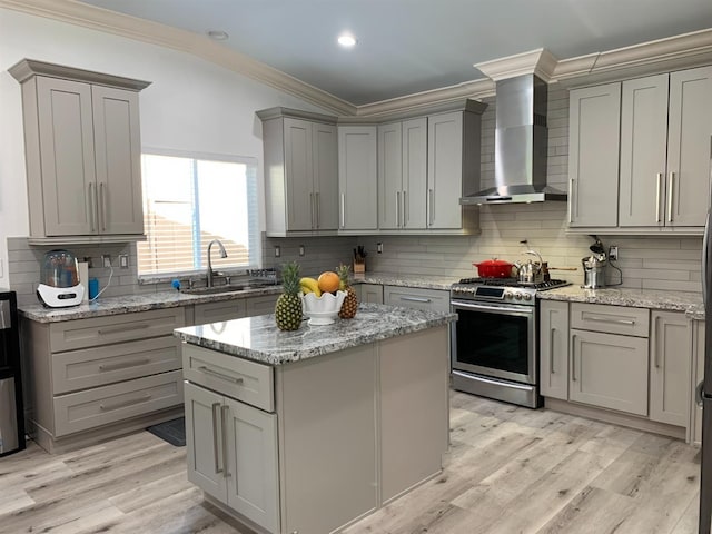 kitchen featuring wall chimney range hood, stainless steel gas range, gray cabinetry, ornamental molding, and backsplash