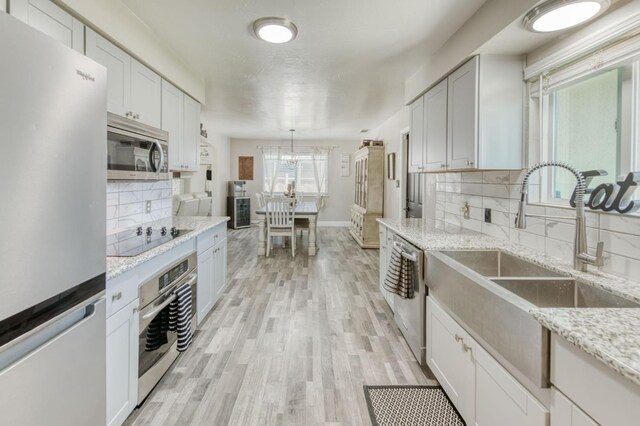 447 W Scott Ave, Clovis, CA 93612 - kitchen featuring appliances with stainless steel finishes, backsplash, light wood-style floors, light stone counters, and white cabinetry