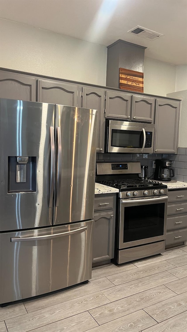 2434 Cherrywood Ct, Hanford, CA 93230 - kitchen featuring stainless steel appliances, gray cabinetry, light wood-style flooring, backsplash, and light stone counters