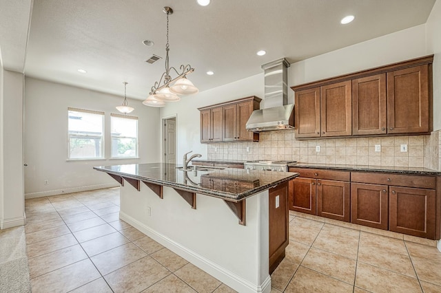 2593 E Utah, Fresno, CA 93720 - kitchen featuring wall chimney range hood, dark stone counters, a kitchen bar, decorative backsplash, and an island with sink