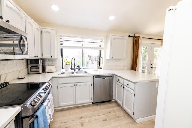 5263 W Griffith Way, Fresno, CA 93722 - kitchen with appliances with stainless steel finishes, backsplash, a peninsula, white cabinets, and light wood-style floors
