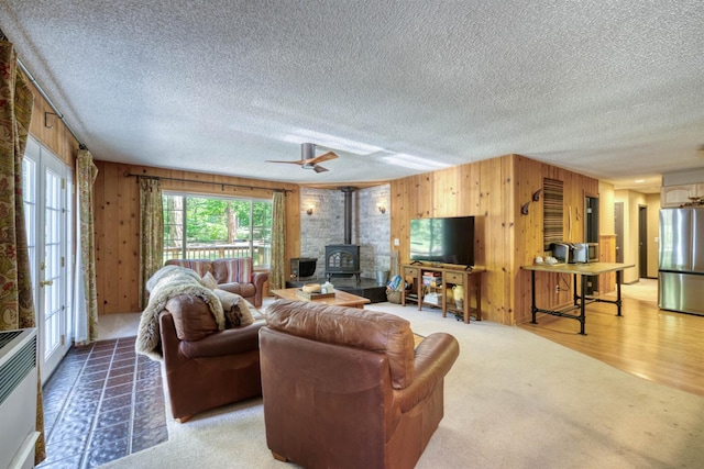 42055 Saddleback Rd, Shaver Lake, CA 93664 - living area with a wood stove, wooden walls, a textured ceiling, and light colored carpet