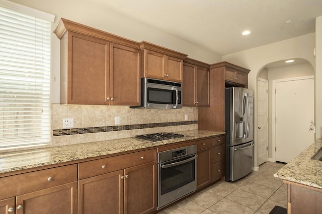 3482 Elevations Way, Clovis, CA 93619 - kitchen with appliances with stainless steel finishes, arched walkways, tasteful backsplash, light stone counters, and light tile patterned floors