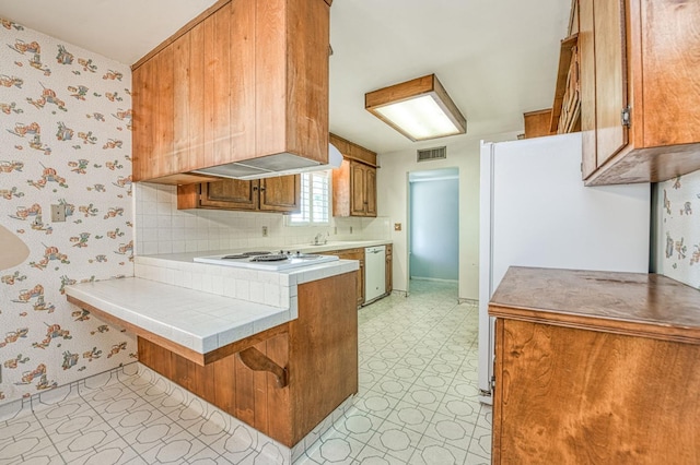 5578 E Perrin Rd, Clovis, CA 93619 - kitchen with white appliances, light floors, a peninsula, wallpapered walls, and brown cabinets
