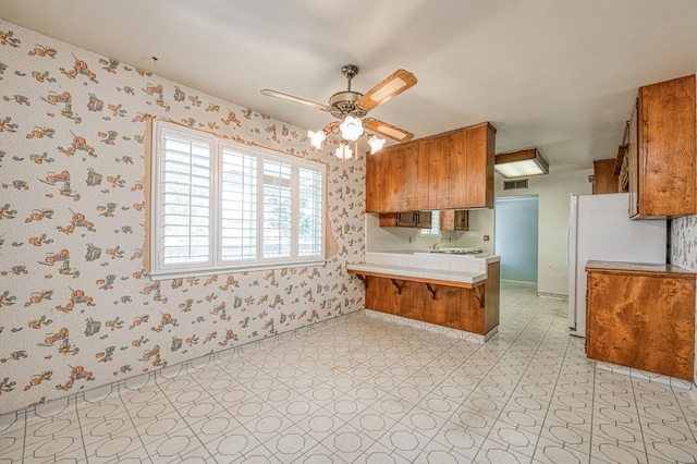 5578 E Perrin Rd, Clovis, CA 93619 - kitchen featuring brown cabinetry, a peninsula, light floors, wallpapered walls, and light countertops