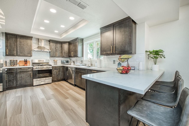 254 W Sierra Ave, Clovis, CA 93612 - kitchen featuring stainless steel appliances, wall chimney exhaust hood, dark brown cabinetry, a peninsula, and a kitchen bar