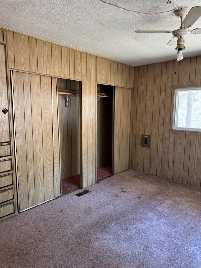 50481 Sundew Rd, Yokuts Valley, CA 93675 - unfurnished bedroom featuring two closets, carpet flooring, wood walls, a ceiling fan, and a textured ceiling