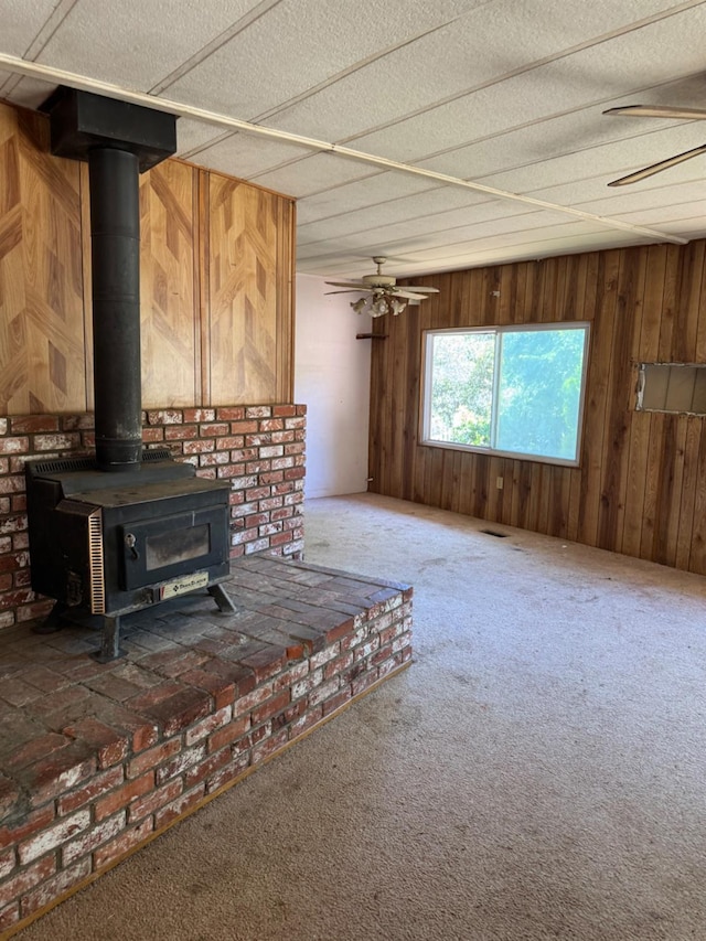 50481 Sundew Rd, Yokuts Valley, CA 93675 - unfurnished living room with carpet flooring, wood walls, a wood stove, and ceiling fan