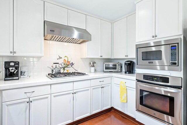 3075 W Silverhill Ln, Fresno, CA 93711 - kitchen featuring ventilation hood, stainless steel appliances, white cabinetry, and tasteful backsplash