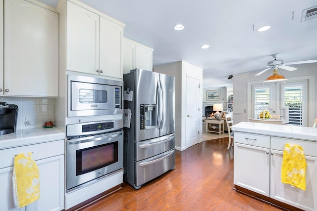 3075 W Silverhill Ln, Fresno, CA 93711 - kitchen featuring stainless steel appliances, tile counters, dark wood-type flooring, white cabinetry, and tasteful backsplash